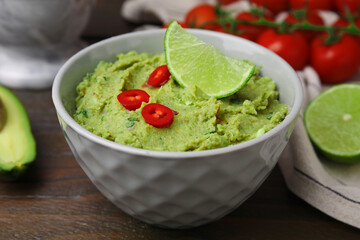 Bowl of delicious guacamole and ingredients on wooden table, closeup