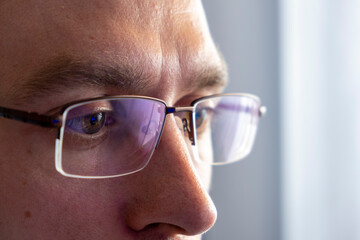 Close up portrait of man in glasses looking in screen of smartphone or laptop or monitor.