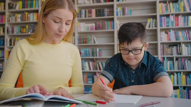 Young inspired experienced teacher educator is engaged in the school education of Down syndrome boy