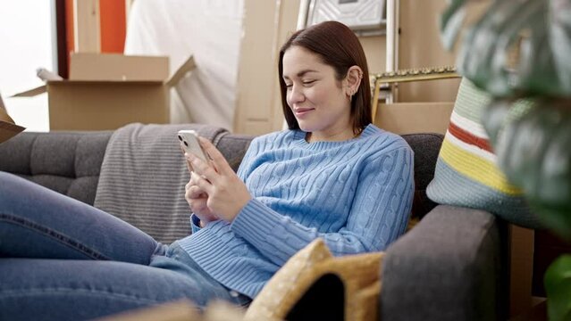Young caucasian woman using smartphone sitting on sofa at new home