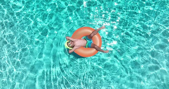 Kid with inflatable ring in swimming pool, top view. Summer vacation. Summer holiday. Summertime kids weekend. Child in swiming pool. Funny boy on inflatable ring at aquapark.