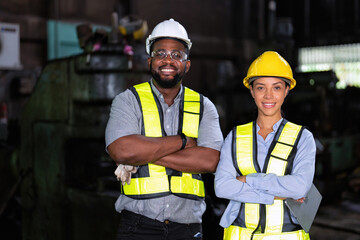 Female worker and coworker posing confidently while standing with arms crossed in factory workshop
