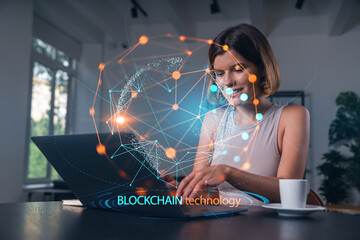 Fototapeta na wymiar Thoughtful businesswoman in casual wear typing on laptop at office workplace with coffee cup. Concept of distant work, business education, internet surfing, information technology. Blockchain hologram