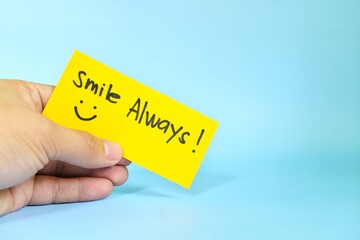 Smile always reminder concept. Hand holding a bright yellow paper message note.