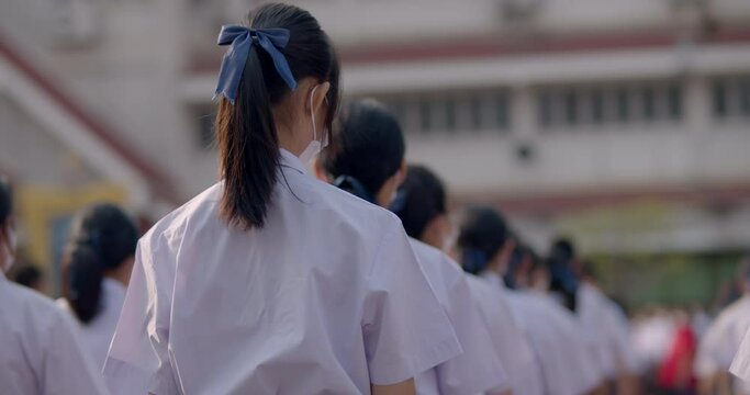 Slow motion scene in the morning while the Asian high school students in white uniform wearing the masks standing in line during the Coronavirus 2019 (Covid-19) epidemic.
