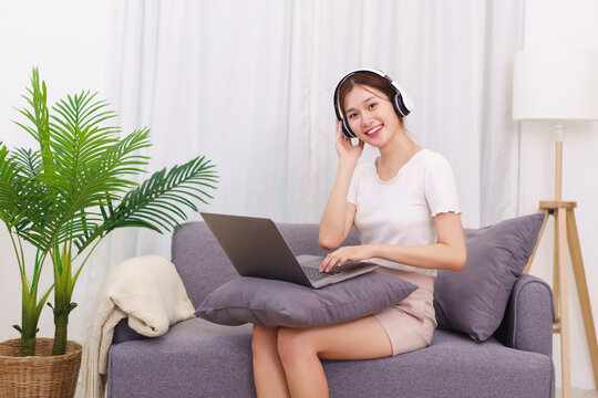 Lifestyle in living room concept, Young Asian woman in headphone to watching movie on laptop