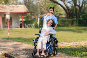 Asian nurse or physiotherapist caring for elderly woman sitting wheelchair. Asian female nurse takes care of patients and takes them for a walk in the hospital park.