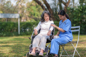 Asian nurse or physiotherapist caring for elderly woman sitting wheelchair. Asian female nurse takes care of patients and takes them for a walk in the hospital park.