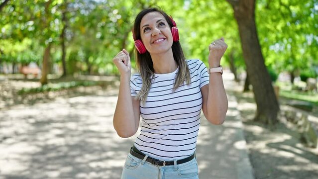 Middle eastern woman dancing listening to music wearing headphones at park