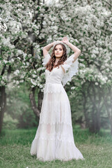 Obraz na płótnie Canvas A beautiful young girl in a white floor-length lace dress in a blooming apple orchard