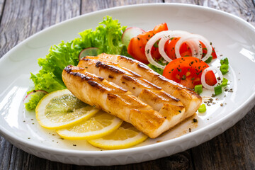 Seared calamari steak with lemon and fresh vegetables on wooden table
