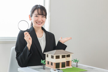 虫眼鏡で模型の家を見る不動産鑑定士・宅建士の女性
