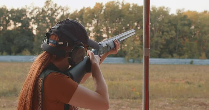 Skeet Shooting Sport. girl in Eye and ear protection practising shooting skeet on field , rare back view, woman in prptective glasses, vest, gear focus on the target want to break clays
