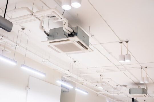 Ceiling mounted cassette type air condition units with other parts of ventilation system with hanging lights and other construction parts.