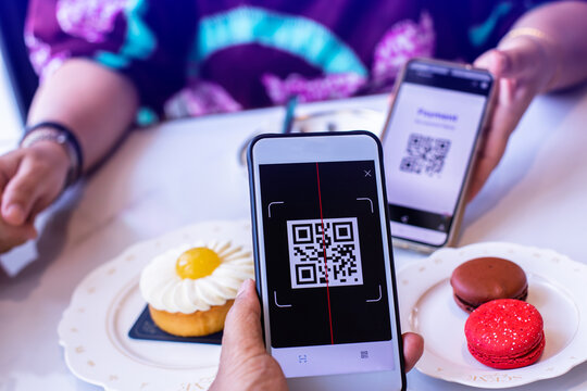 Customer hand using smart phone to scan QR code tag with blur  colourful macaroons cakes of different colors in coffee shop or restaurant to accepted generate digital pay without money. Qr code paymen