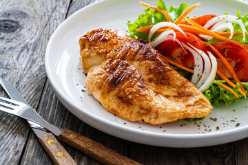 Grilled chicken breast and fresh vegetables on wooden table
