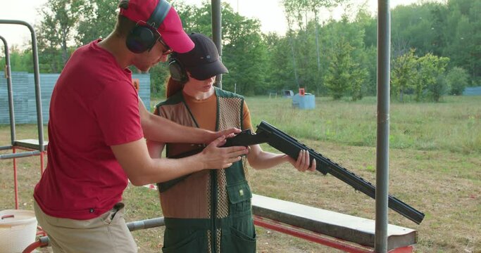 young couple wearing protective safety goggles headsets caps.is on a sporting clays course, classes, young man instructor explaining woman how to shoot clay disc, bird, lifestyle hobby interests