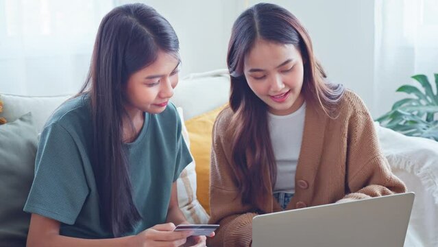 Excited happy two roommates shopping online together with mockup credit card and laptop sitting on a sofa at home, Online payment, easy and digital payment for ecommerce