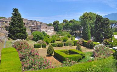 Landscaped garden with cut hedge and trees in the town of Pompeii with the ruins in the background - Italie