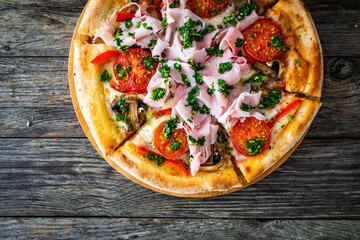 Pizza with cooked ham, mozzarella cheese and vegetables on wooden table