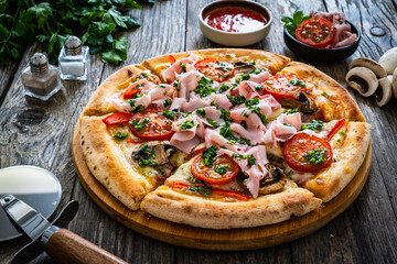 Pizza with cooked ham, mozzarella cheese and vegetables on wooden table