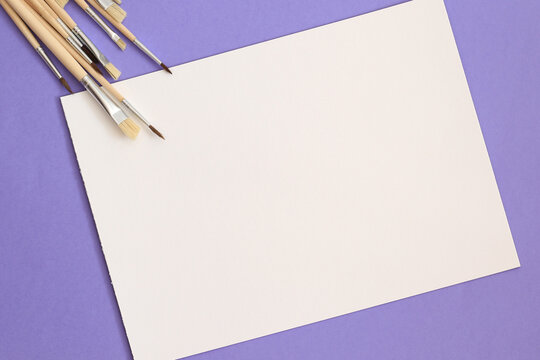 empty white paper sheet on purple background with aquarelle brushes