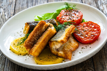 Seared eel steaks and fried tomatoes served on wooden table
