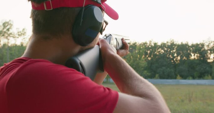 Skeet Shooting Sport. young adult man is shooting during a skeet competition, back rare view. Man shooting skeet with a shotgun. gunman shooting asphalt pigeon