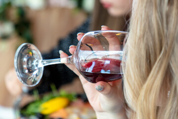 Woman drinking wine in restaurant. Closeup of female hands holding glass of wine