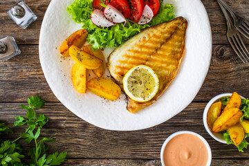 Grilled sea bream with potatoes and fresh vegetables on wooden table
