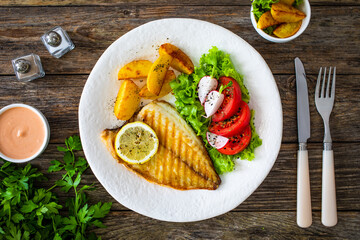 Grilled sea bream with potatoes and fresh vegetables on wooden table
