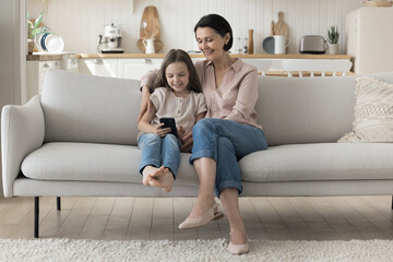 Happy loving grandmother taking care of preschool little grandkid girl. Child using mobile phone at...