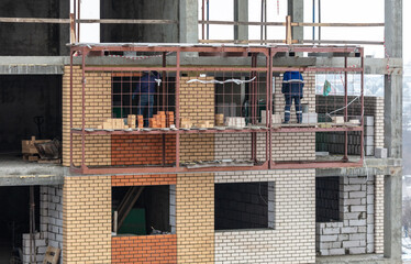 Workers lay brick walls at the construction site of a multi-storey building.