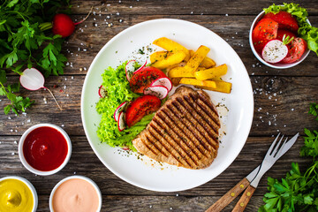 Grilled beef steaks with fresh vegetable salad and French fries on wooden table
