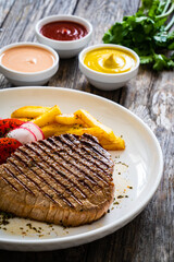 Grilled beef steaks with fresh vegetable salad and French fries on wooden table

