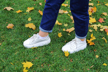 Female legs in white sneakers on the background of autumn leaves