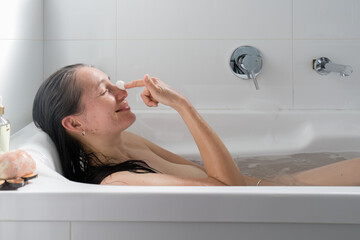 Relaxed woman gently exfoliating dead skin from her face using silkworm cocoon. Concept of self-care. 