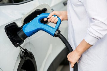 Young business woman refueling her electric car at a EV charging station. Concept of environmentally friendly vehicle. Electric car concept. Green travelling.