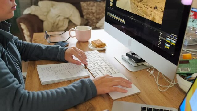 Young woman in cozy home environment sits at desk in front computer next to devices and cup of tea with cookies work at home. Productivity and efficiency in workplace