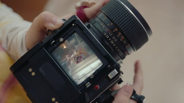 Hands of woman turning shutter cocking lever of camera, photographing her boyfriend sitting at home, focus on camera body and viewfinder. Close-up shot