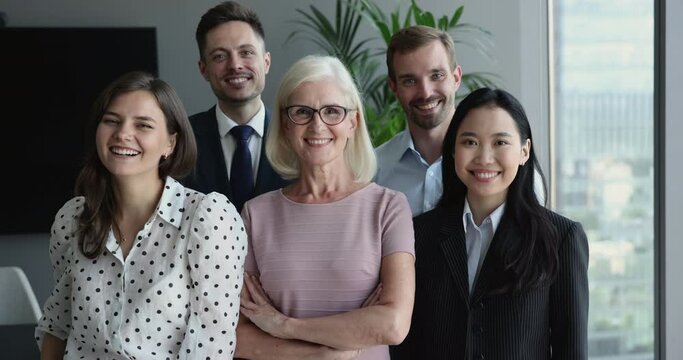 Diverse business team of serious young millennial colleagues and confident senior business leader posing in office, getting happy, cheerful, celebrating success, looking at camera. Front view