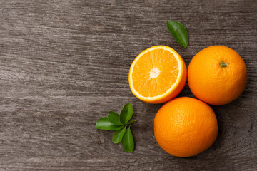 Orange fruit with cut in half sliced and green leaves on wooden table background, top view, flat lay.