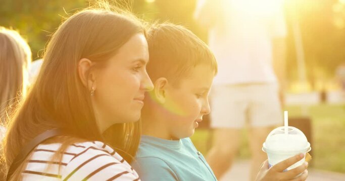 Child and mom have fun in the park, child eats hotdog and drinks milkshake.