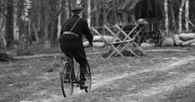 Re-enactor Dressed As Nkvd Forces Rides A Bike. Peoples Commissariat For Internal Affairs, Abbreviated Nkvd, Was Interior Ministry Of The Soviet Union. Black And White Video.