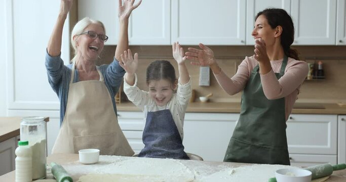 Happy multigenerational relatives women having fun throwing flour while prepare dough for homemade pie or cookies laughing enjoy communication and cookery together on weekend. Friendly family pastime
