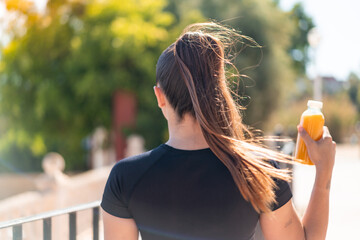 Young pretty sport woman holding an orange juice at outdoors in back position