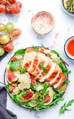 Gourmet salad with fresh figs and grilled chicken fillet, grape, arugula, chard with wine vinegar dressing. White kitchen table background, top view