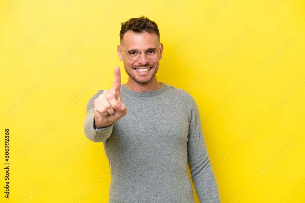 Wall mural Young caucasian handsome man isolated on yellow background showing and lifting a finger