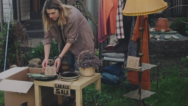 Garage sale. Young woman puts price sign for second hand items.