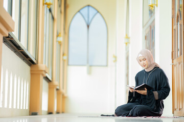 The image of an Asian Muslim woman in the Islamic religion in hijab in cream and black color. reading the Quran and having a happy smiling face Staying in a beautiful mosque out of respect for God.